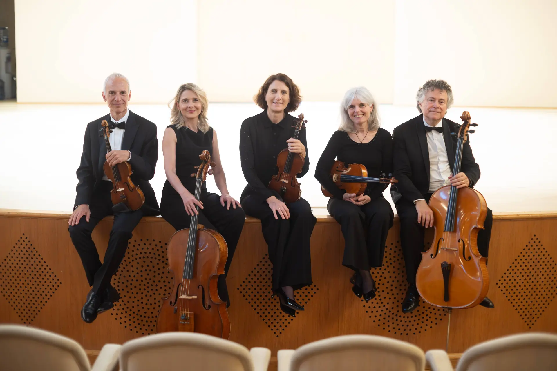 Il Nuovo Quintetto Boccherini seduto sul bordo del palco con gli strumenti, le poltrone della sala in primo piano